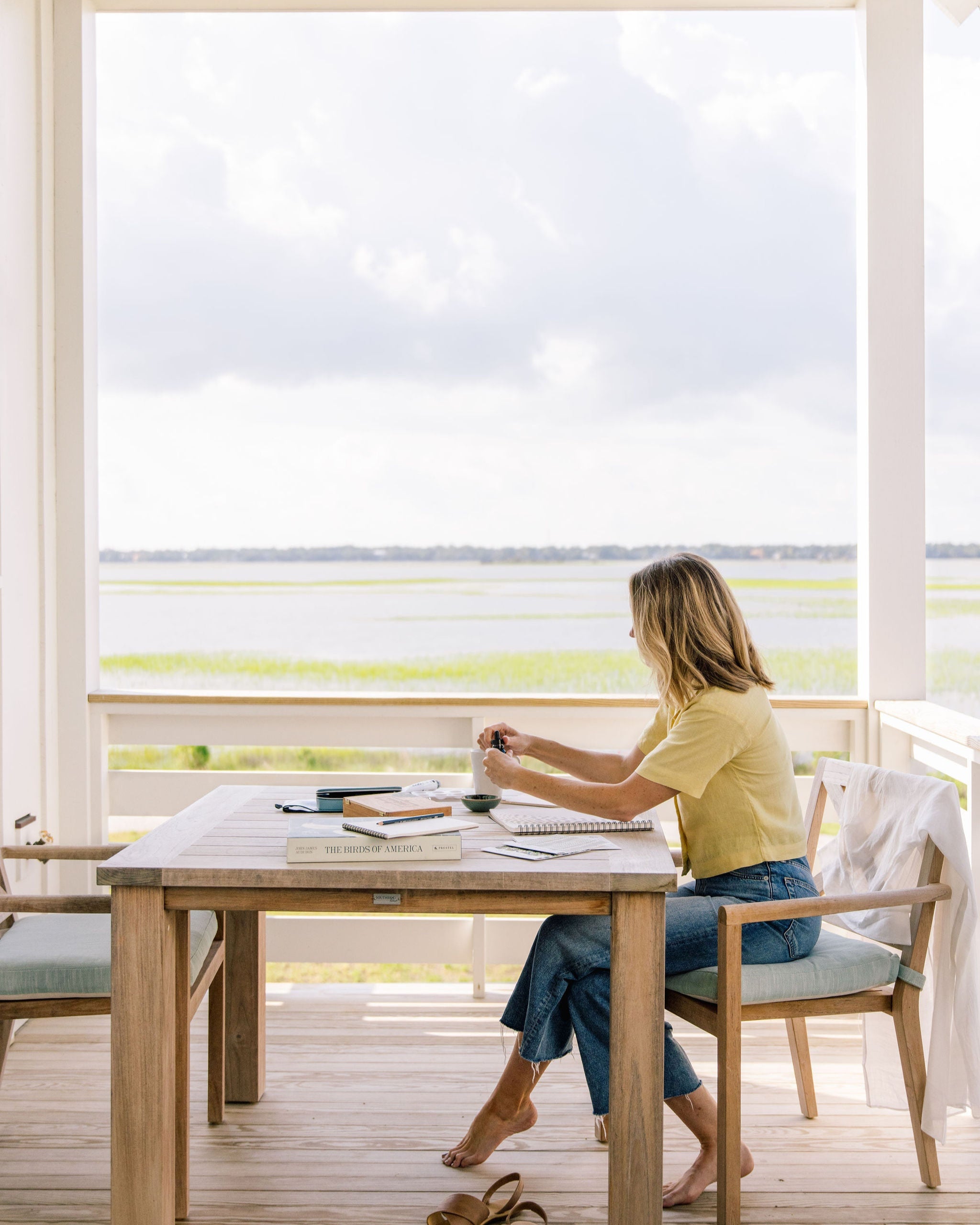 Woman sitting at a table by large windows with a scenic view.