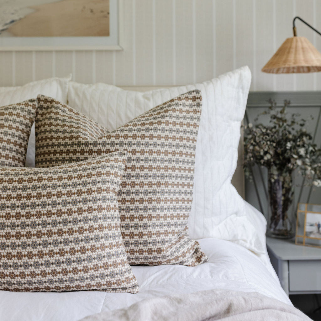 Neutral Emily Daws pillows arranged on a bed, styled to highlight small-batch fabrics and bespoke interiors.