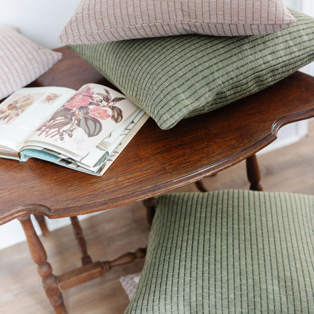 Emily Daws Jetty Palm green pillows styled on a wood table, boutique woven fabrics for high-end interiors and bespoke window treatments.
