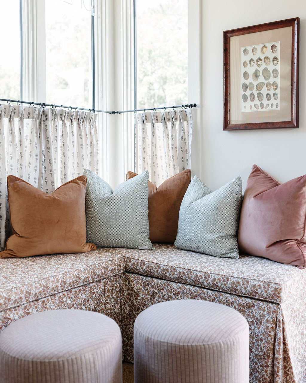 Sectional sofa with patterned cushions and matching ottomans in a room with large windows and a framed picture on the wall.