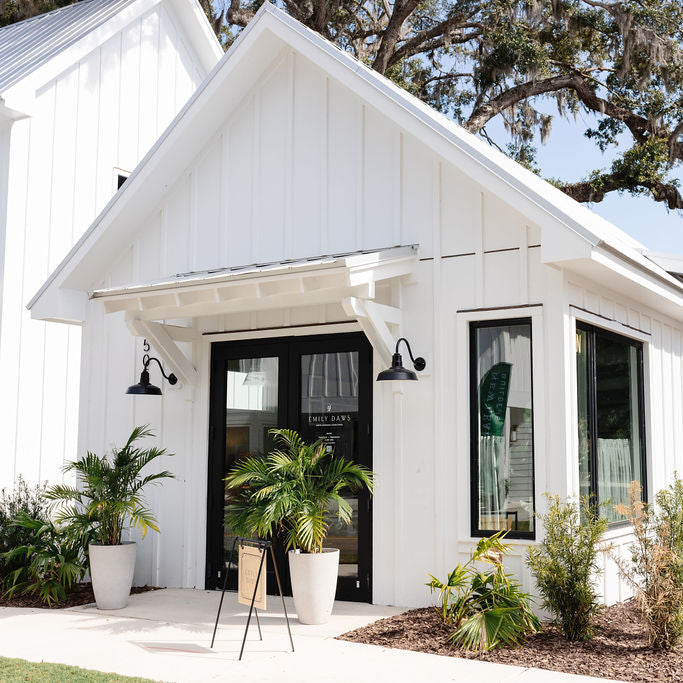 White house exterior with black door and windows, potted plants, and a clear sky.