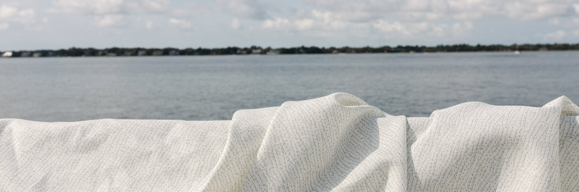 Emily Daws "Harbor" fabric draped over a railing with the Charleston Harbor and cloudy sky in the background