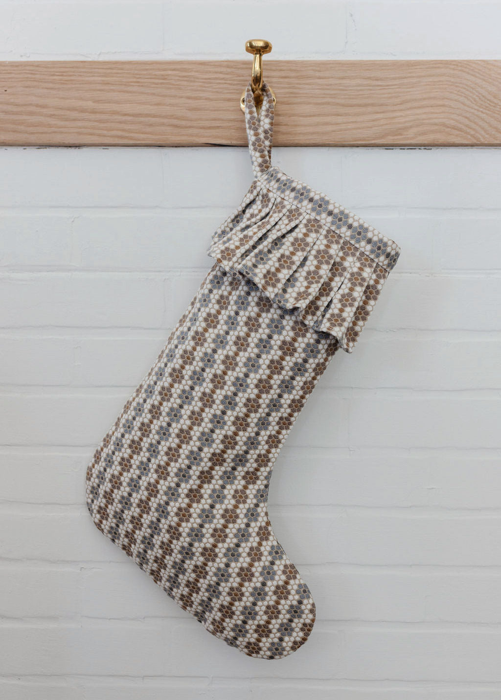 A neutral woven holiday stocking in Emily Daws’ Nectar pattern hanging against a white shiplap wall.