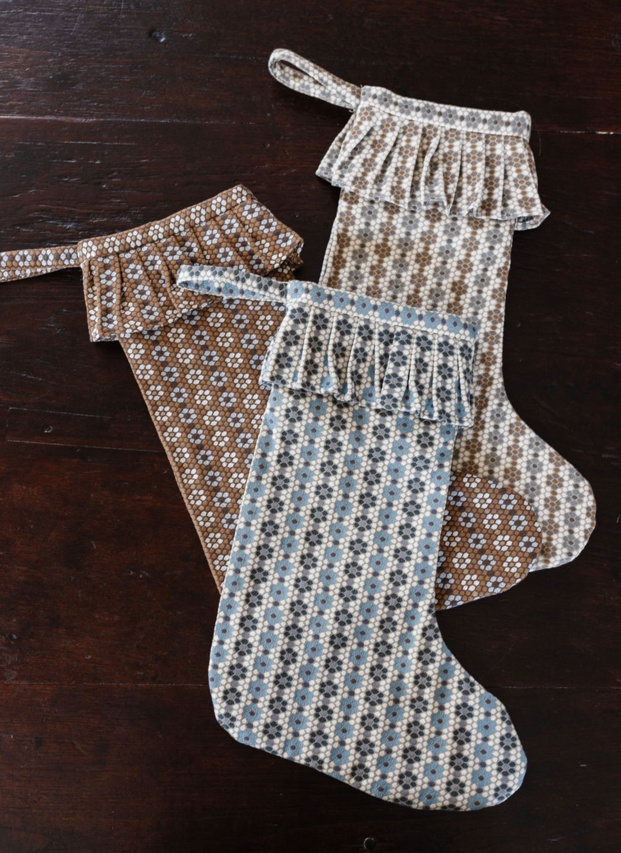 Three woven holiday stockings made from Emily Daws’ Nectar pattern in assorted colorways, displayed on a dark wood tabletop.