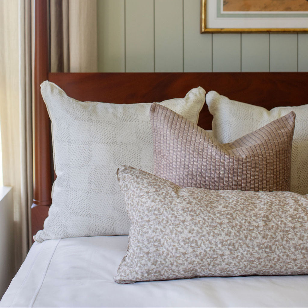 Neutral Emily Daws pillows arranged on a bed, styled to highlight small-batch fabrics and bespoke interiors.