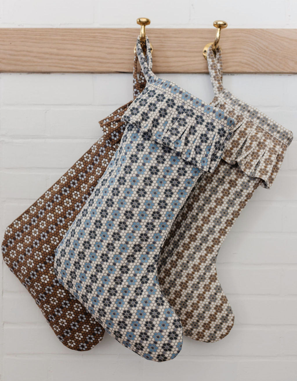 Three woven Nectar-pattern holiday stockings in coordinating colorways hanging together on brass hooks.