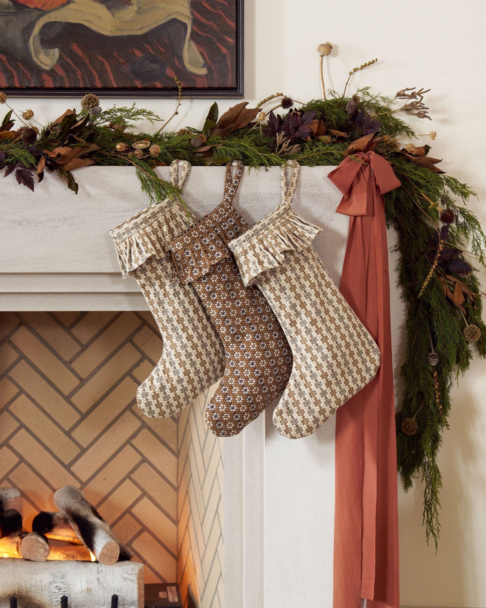 A festive fireplace mantel decorated for the holidays with woven Nectar-pattern stockings hanging from brass hooks.