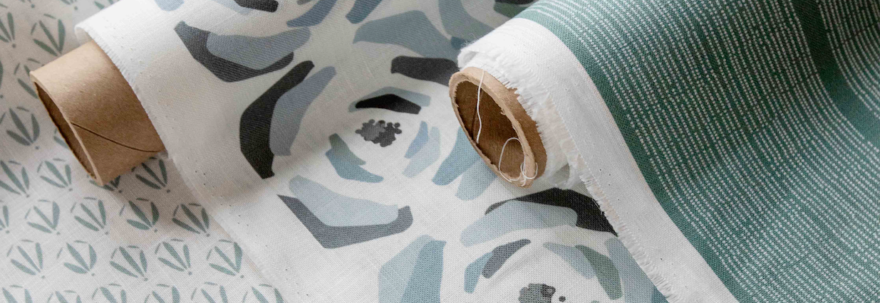 Two rolls of patterned linen fabric with floral designs on a textured surface.