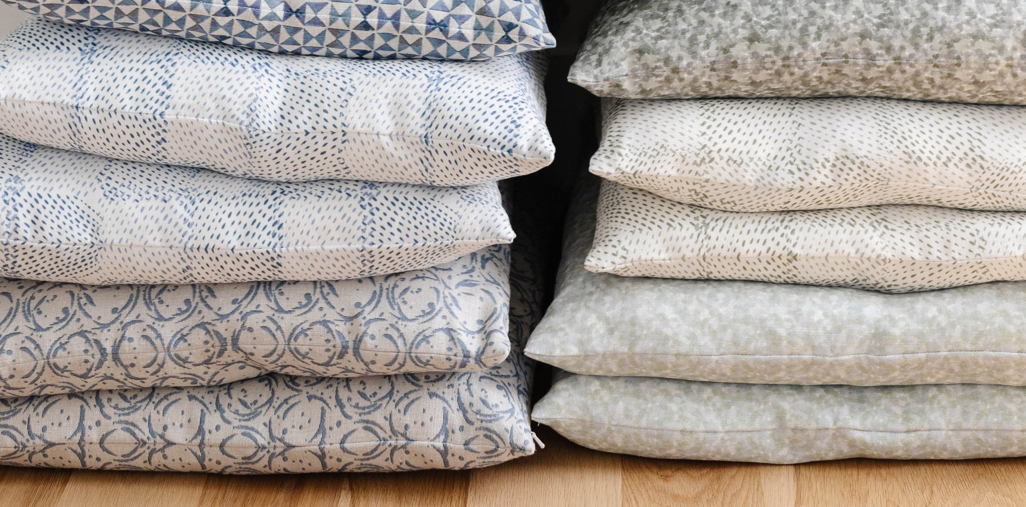 Stacks of Emily Daws patterned and printed linen throw pillows on a wooden floor.