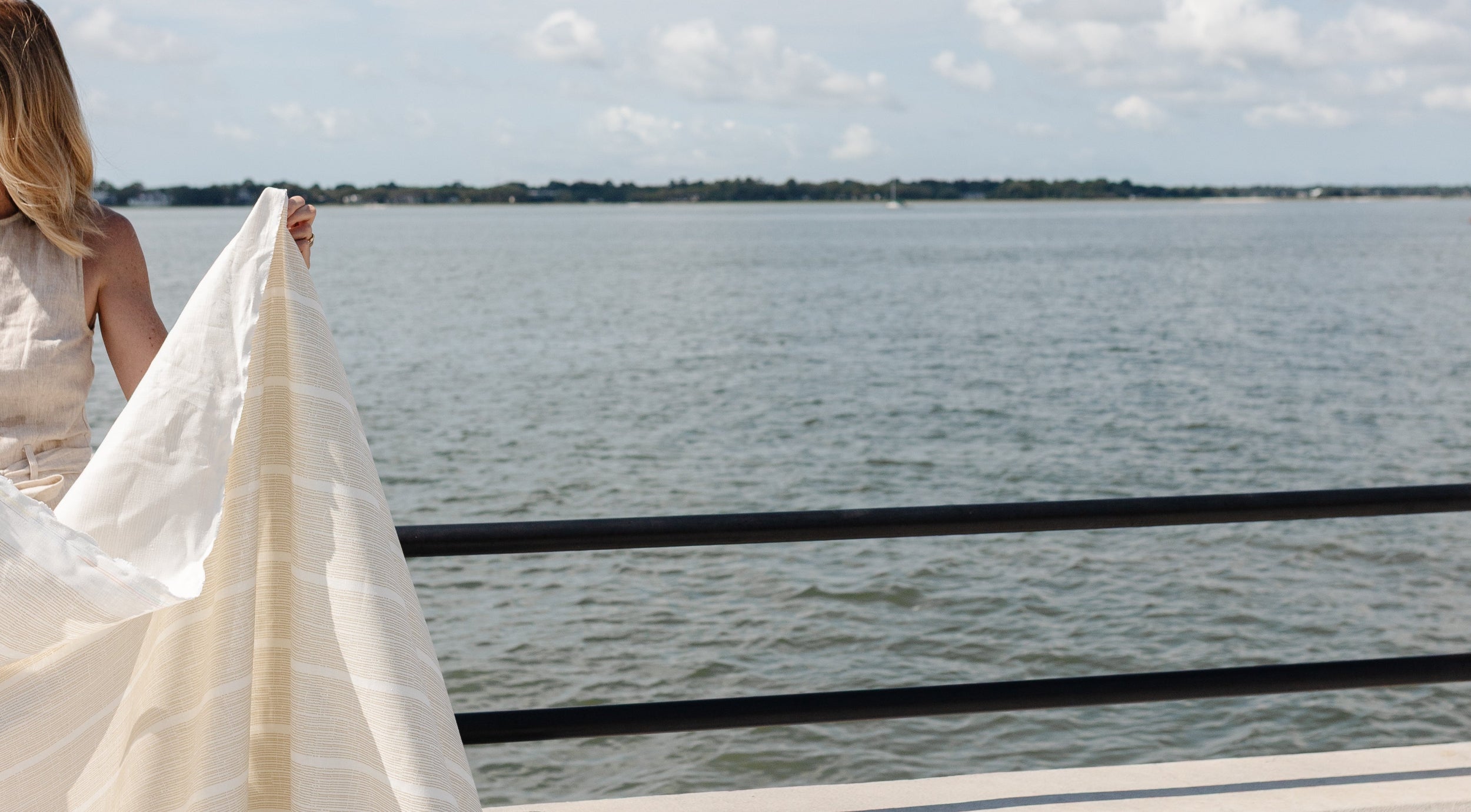 Emily Daws holding printed linen fabric by a railing with the Charleston harbor in the background.