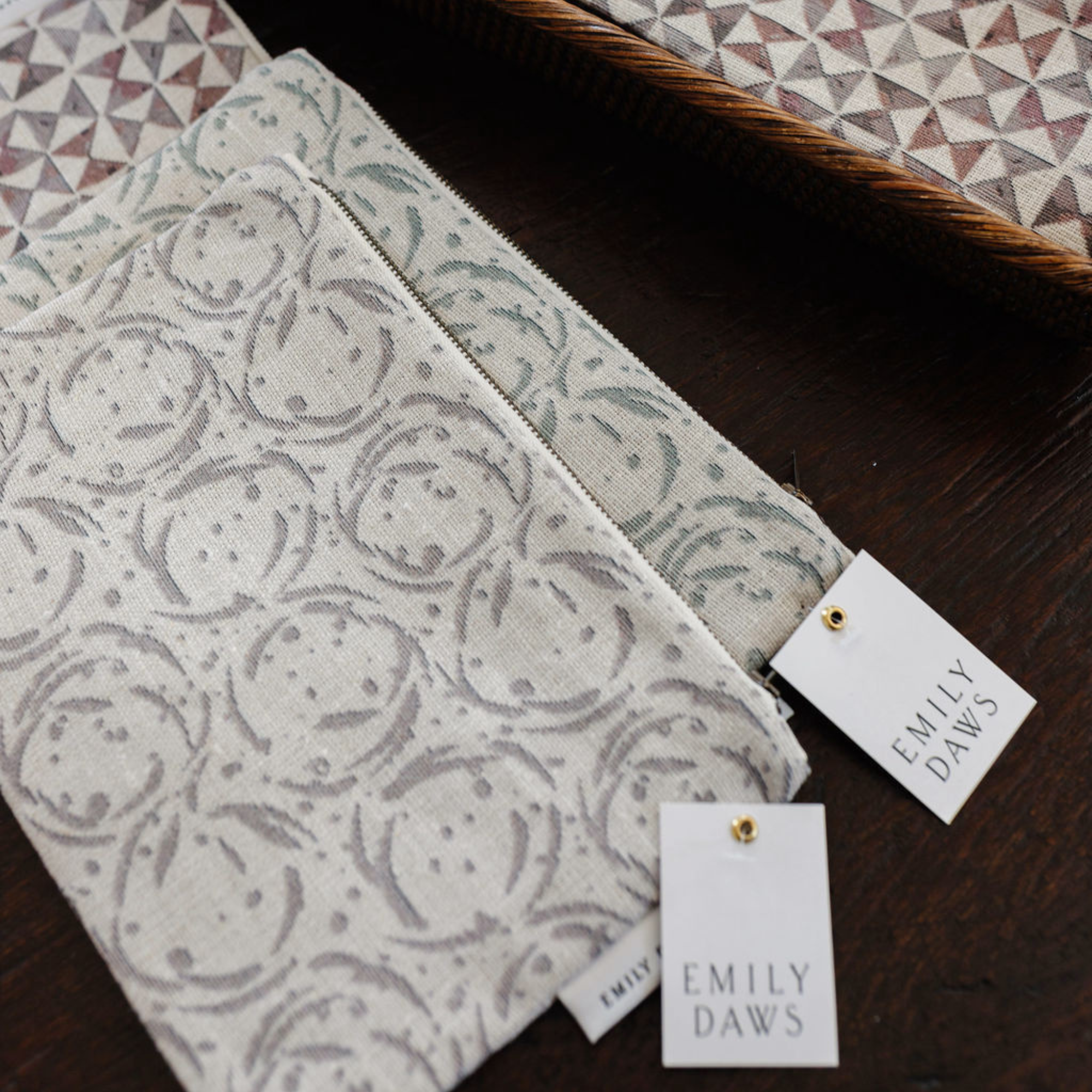 Two linen zipper pouches with a geometric pattern, one displayed in a folded position showing the pouch's design, and the other laid flat showing the reverse side. Both pouches have a tag with the brand name 'Emily Daws Textiles'.