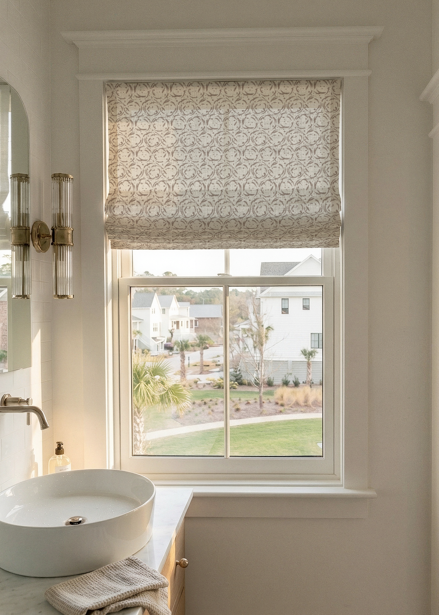 Bathroom window with a view of a residential area, featuring decorative wall sconces and a Roman shade in Nest fabric in Nutmeg by Emily Daws.