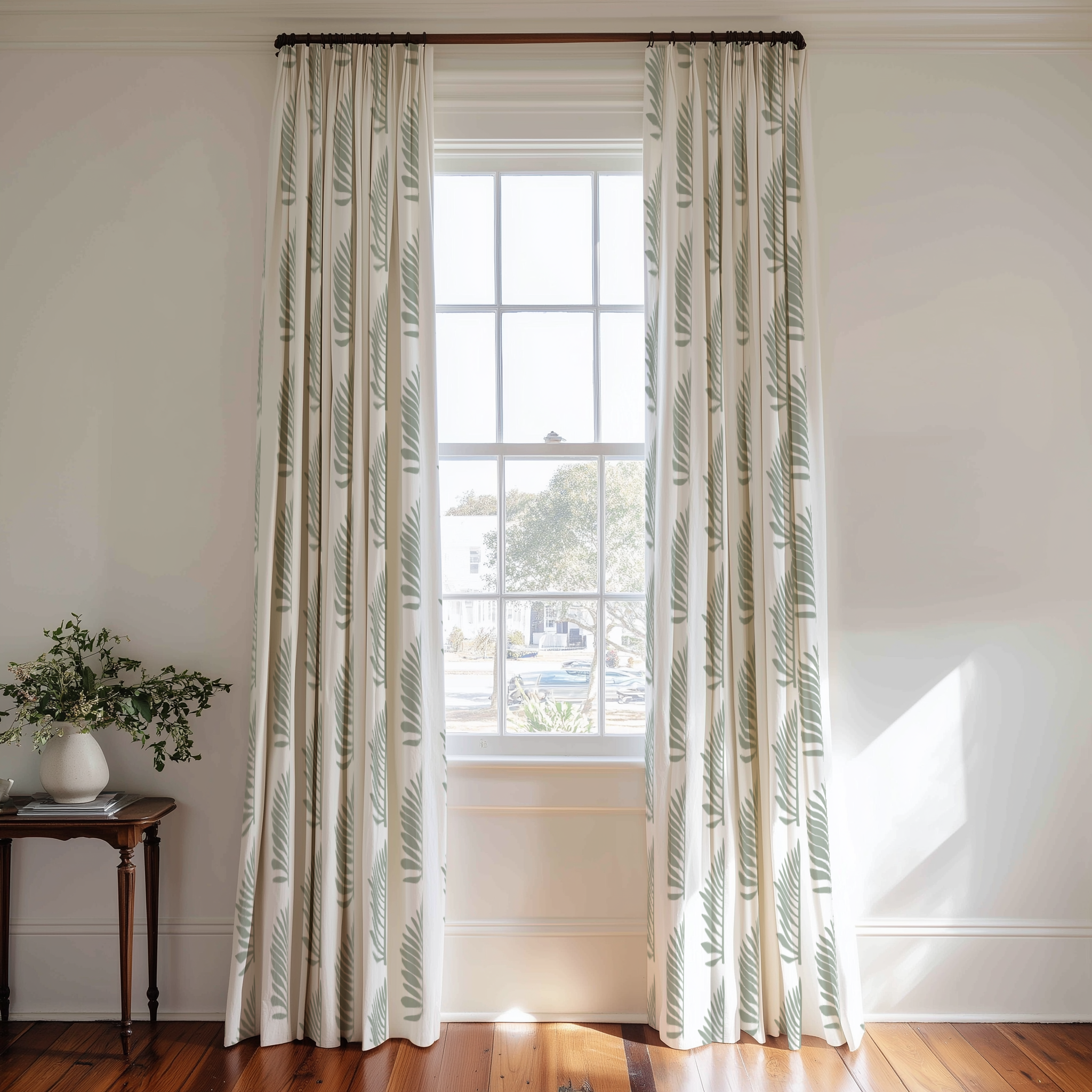 Window with white curtains featuring green leaf Palmetto pattern by Emily Daws wooden side table with plant, and white walls.